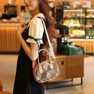 Pink check pattern Boston handbag with wide shoulder strap worn by model in a cafe