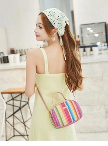 Detail of colorful striped woven crossbody bag with pink handle and gold metal plaque