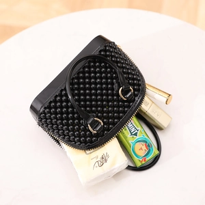 Mini black beaded shell jelly bag with golden rings and zipper on marble base