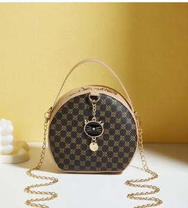 Detail of round crossbody bag featuring gold clover pattern and black cat metal charm