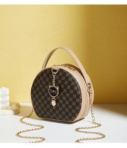 Close-up of circular handbag with clover pattern, gold chain and cat charm detail