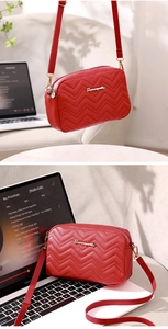 Detail of red quilted crossbody bag with golden logo placed on a laptop keyboard