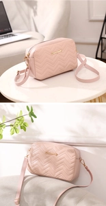 Detail of light pink wave-quilted crossbody bag with golden logo on marble tabletop