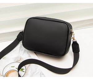 Detail shot of black leather camera bag with wide fabric strap and gold-tone metal zippers