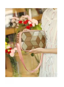 Detail view of a geometric patchwork camera bag with wide pink fabric strap and gold logo