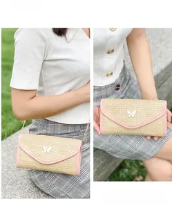 Detail of woven straw envelope bag with pink trim and butterfly clasp on a gold chain