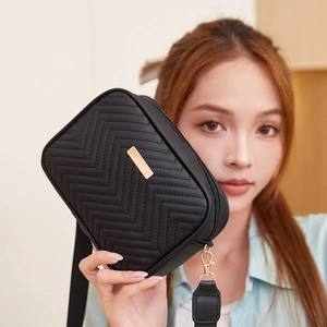 Black quilted crossbody camera bag with wave pattern and wide strap held by model