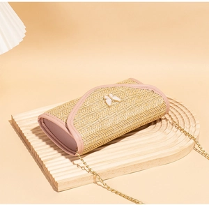 Detail of woven straw envelope bag with pink trim, golden chain, and butterfly ornament