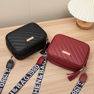 Quilted crossbody bags in black and burgundy with wide logo straps on a wooden table