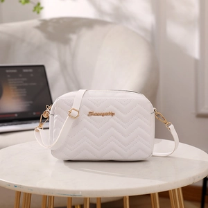 Elegant white quilted crossbody bag with golden logo on marble table in a modern setting