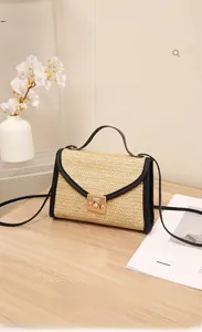 Detail of straw woven bag featuring black leather trim and golden metal lock on wooden table