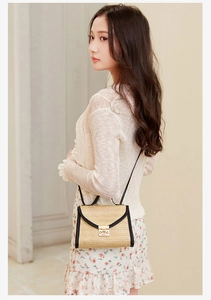 Detail of minimalist straw woven crossbody bag featuring black leather trim and gold metal lock