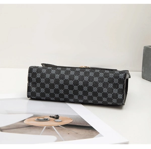 Détail du sac à bandoulière gris foncé structuré avec motif trèfle sur un magazine