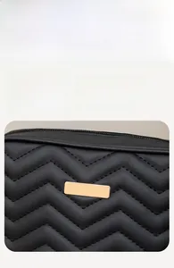 Detail of black quilted leather camera bag with V-shaped stitching and gold metal plate