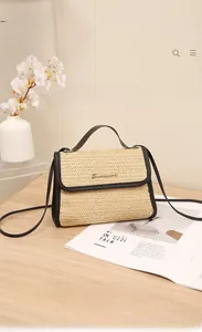 Detailed view of straw crossbody bag with black leather trim and golden logo on wooden table