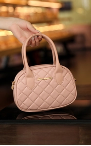 Close-up of pink quilted leather pillow bag with gold heart charm and brand logo