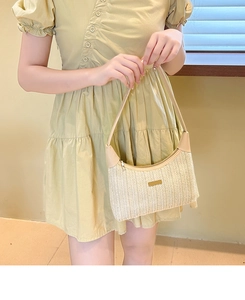 Detail of woven straw shoulder bag with beige leather trim and metal logo plate
