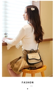 Straw and black leather contrast crossbody saddle bag shown in a cozy cafe setting