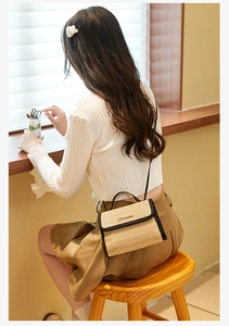 Straw mini crossbody bag with black leather trim worn by a model in a cozy cafe