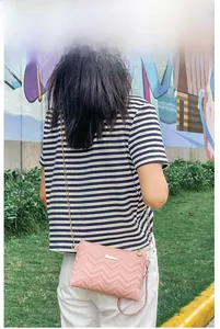 Pink crossbody bag with wave embroidery and gold chain strap worn by a model outdoors