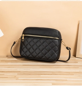 Close-up of black quilted crossbody camera bag with elegant gold hardware on wooden surface