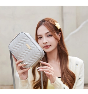 Detail of grey crossbody bag with wavy quilting and elegant gold metal plate
