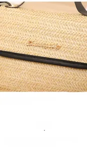 Detailed view of woven straw texture with black faux leather trim and gold logo hardware