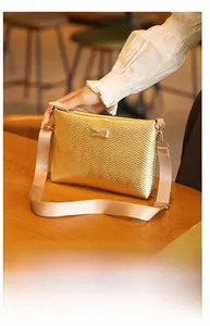 Detail of golden crossbody bag with wave texture and wide nylon shoulder strap on wood table