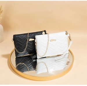 Detail of black and white quilted clutches with golden chains on a mirrored surface