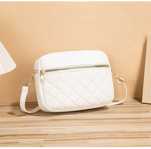 Macro shot of white quilted crossbody bag with golden hardware on a wooden table