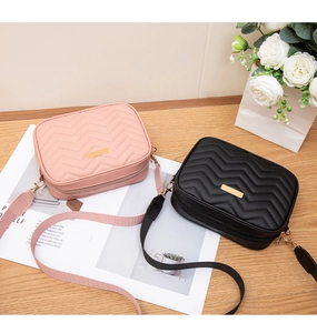 Detail view of pink and black quilted crossbody bags with wide straps on a wooden table