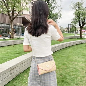 Women's woven straw crossbody bag with pink trim and white butterfly ornament on the flap