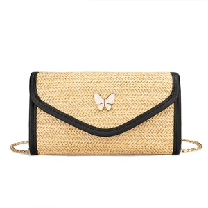 Minimalist straw woven crossbody bag with black trim, butterfly detail, and gold chain strap
