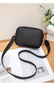 Detail of black rectangular camera bag with gold hardware and wide fabric strap