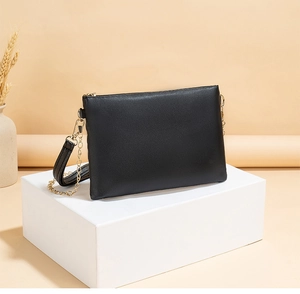 Detail of black crossbody bag with wave embroidery, gold chain, and leather strap
