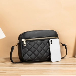 Borsa a tracolla trapuntata nera con cerniera dorata accanto a uno smartphone bianco
