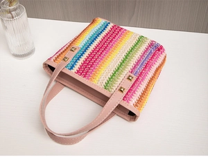 Dettaglio borsa in paglia intrecciata multicolore con manici in pelle rosa e borchie