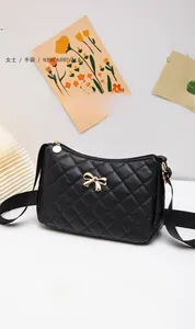 Detail of black quilted shoulder bag featuring golden bow hardware and nylon strap