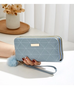 Détail du portefeuille long matelassé bleu clair avec double zip et pompon en peluche
