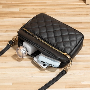 Borsa a tracolla nera trapuntata con finiture dorate su sfondo in legno chiaro