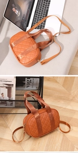 Detail of orange-brown quilted Boston bag featuring wide fabric handles and gold zipper