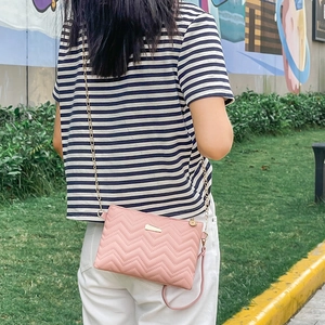 Pink wavy quilted crossbody bag with gold chain strap shown on model outdoors