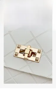 Detailed close-up of golden rectangle twist lock and quilted pattern on white crossbody bag