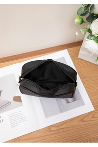 Top view of black textured leather cosmetic bag with gold zipper and D-ring on a magazine