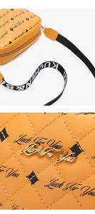 Detail of yellow quilted camera bag with Luck For You text and logo on white background