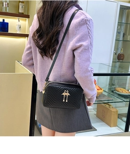 Side view of black quilted crossbody bag with golden bird emblem and fringe detail
