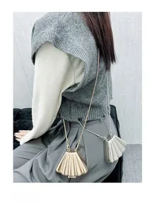 Close-up of gold and silver shell-shaped mini bags with chain straps on a model