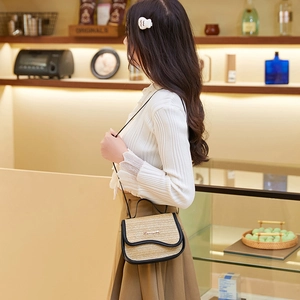 Straw crossbody bag with black leather trim and metal logo on warm indoor background