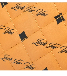Macro shot of orange leather crossbody bag featuring diamond quilting and Luck For You print
