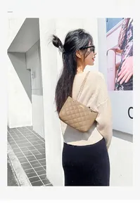 Detail of khaki quilted crossbody bag with golden chain strap on a female model